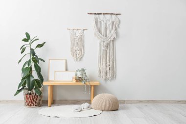 Ahşap bank, puf, fotoğraf çerçeveleri ve salonun iç tarafındaki beyaz duvarın yanındaki bitkiler.