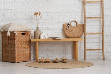 Tahta bank, hasır sepet, ayakkabılar ve merdiven salonun içindeki beyaz tuğla duvarın yanında, yakın plan.