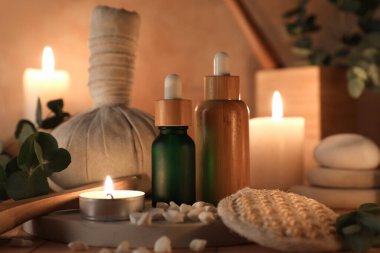 Bej arka planda yanan mumlar, kozmetik ürünler şişeleri ve bitkisel poşet, yakın plan.