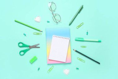 Turkuaz arka plan üzerine gözlüklü, not defterli ve okul malzemeli kompozisyon