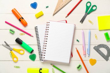 Beyaz ahşap zemin üzerine boş defterler ve kırtasiye malzemeleri içeren kompozisyon, yakın plan