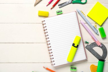 Beyaz ahşap zemin üzerine boş defter ve kırtasiye malzemesi içeren kompozisyon, yakın plan