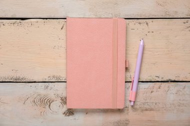 Bej ahşap arka planda pembe defter ve kalemle kompozisyon, yakın plan