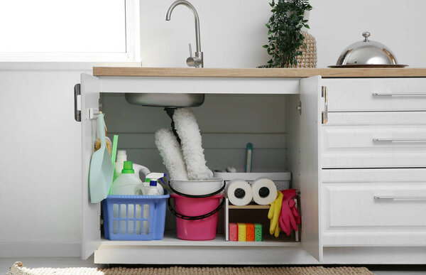 Baskets and bucket with different cleaning supplies and paper towels under sink in kitchen