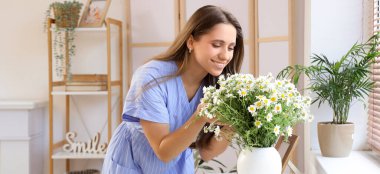 Oturma odasındaki tuvalette papatya çayı ve vazo taşıyan genç bir kadın.