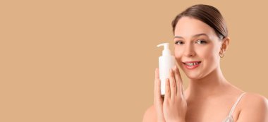 Bej arka planda cilt bakımı ürünü şişesi olan genç bir kadın.