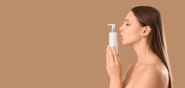 Bej arka planda cilt bakımı ürünü şişesi olan genç bir kadın.