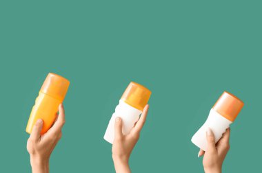 Yeşil arka planda güneş kremi şişeleri olan kadın elleri