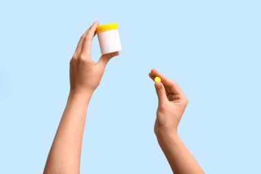 Mavi arka planda ilaç şişesi tutan kadın eller.