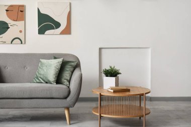 Aydınlık oturma odasının içinde şık bir kanepe, resimler ve masa var.