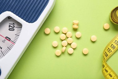 Kilo kaybı hapları, teraziler ve yeşil arka planda mezura.