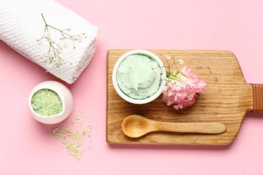 Pembe arka planda bir kase vücut fırçası, deniz tuzu ve temiz havluyla kompozisyon