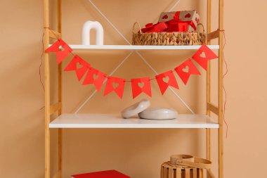 Bej duvarın yakınındaki kitaplıkta asılı kalpleri olan bir kiraz kuşu. Sevgililer Günü kutlaması