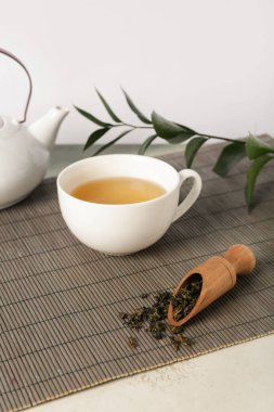 Çaydanlıklı bambu hasırı, bir fincan çay ve beyaz arka plandaki grunge masasında yapraklar.