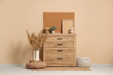 Çekmeceler, otlar, puf ve çerçeveler bej duvarın yanında.