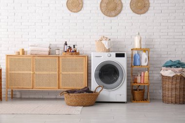 Modern çamaşır makinesi, sepetler, çamaşır deterjanı ve çekmeceli raf ünitesi.