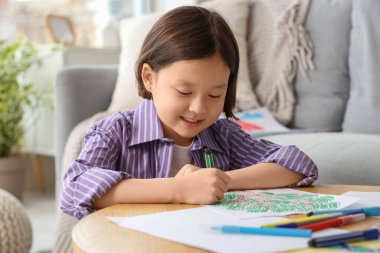 Evdeki masada güzel bir Asyalı kız çiziyor.