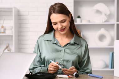 Genç diyabetik kadın ofisinde tükenmez kalemle kan örneği alıyor.