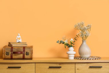Çantalı çekmeceler, vazolarda çiçekler ve odada turuncu duvarın yanında dekor. Yakın çekim.