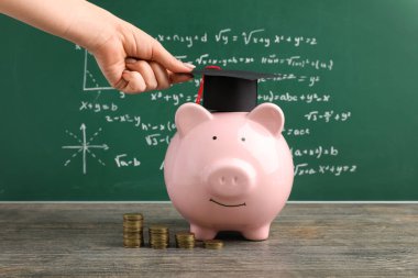 Mezuniyet şapkasını yeşil karatahtanın yanındaki kumbara üzerine koyan kadın. Öğrenci kredisi kavramı