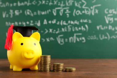 Mezuniyet şapkası ve bozuk paralarla yeşil tahtanın yanındaki masada kumbarada. Öğrenci kredisi kavramı