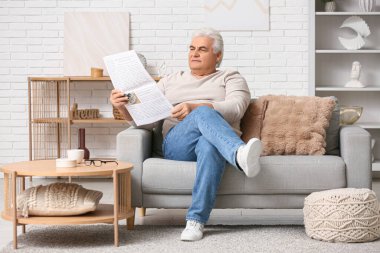 Yakışıklı son sınıf öğrencisi gazete okuyor ve oturma odasında kanepede oturuyor.