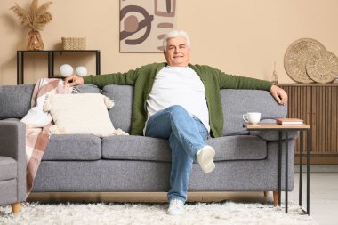 Oturma odasında kanepede oturan mutlu kıdemli adam.