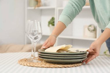 Genç bir kadın evdeki yemek masasına temiz tabaklar koyuyor, yakın plan.