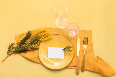 Boş bir kart ve sarı arka planda mimoza çiçekleri olan güzel bir masa.