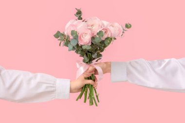 Bir buket ranunculus çiçeği ve pembe arka planda okaliptüs olan kadın elleri.