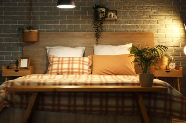 Gece yatak odasının iç tarafındaki gri tuğla duvarın yanında büyük, rahat yatak ve komodinli masalar.