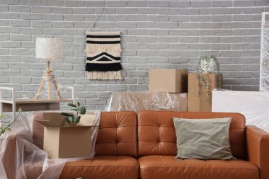 Üzerinde film ve karton kutu olan kahverengi kanepe taşınma gününde oturma odasında.