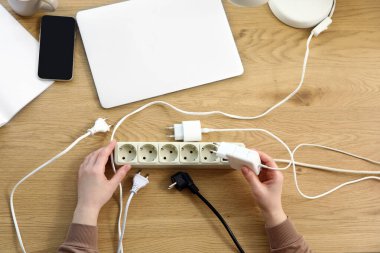 Kadın eller, uzatma kablosundan şarj aletini ahşap sehpanın üstüne çıkarıyor. Ulusal Fişi Çıkarma Günü