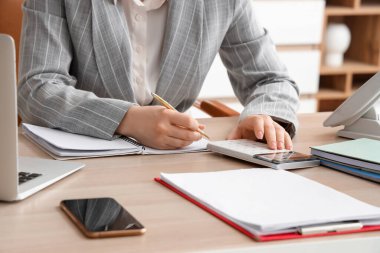 Hesap makinesi ve kadın muhasebeci masada deftere yazı yazıyorlar.