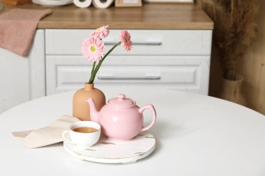 Pembe çaydanlık, bir fincan çay ve mutfaktaki masada güzel çiçekler.
