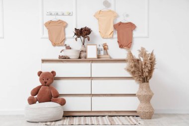 Klozet, puf ve asılı bebek kıyafetleri olan bir kreş.