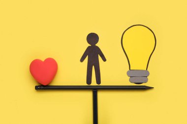 Kağıt ampullü insan silueti ve sarı arka plandaki kalemlerden yapılmış pullarda kalp. Mantık kavramı
