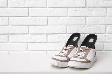 Beyaz tuğla duvarın yanındaki bankta ortopedik tabanlı spor ayakkabılar.