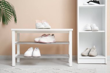 Koridordaki bej duvarın yanındaki bankta ortopedik tabanlı spor ayakkabılar.