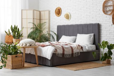 Yatak odasının içi bençle, katlanır ekranla ve hasır sepetlerde bitkilerle dolu.