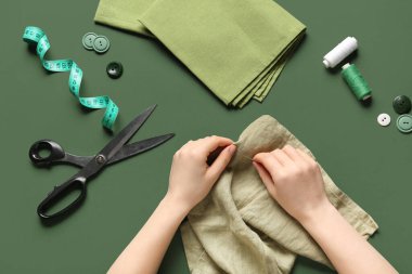 Kadın elleri yeşil arka planda elbise dikiyor.