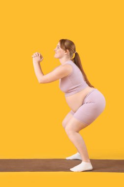 Sportif genç hamile kadın sarı arka planda yoga minderi eğitimi alıyor.