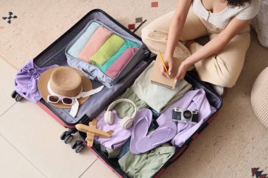 Bavulu olan genç bir kadın yatak odasına gitmek için toplanacak eşyaların listesini yazıyor.