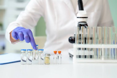 Ampule ve mikroskobu olan kadın bilim adamı laboratuarda, yakın planda.