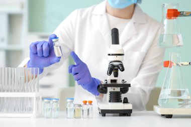 Ampule ve mikroskobu olan kadın bilim adamı laboratuarda, yakın planda.