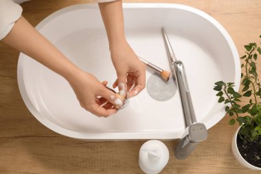 Kadın elleri makyaj fırçasını lavabonun üstünde yıkıyor.