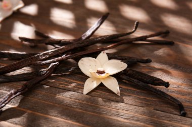 Vanilya çubukları ve çiçek ahşap arka planda, yakın plan