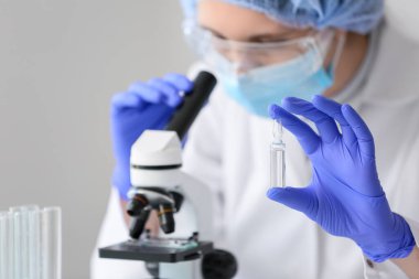 Ampulü olan kadın bilim adamı laboratuarda mikroskoptan bakıyor, yakın plan.