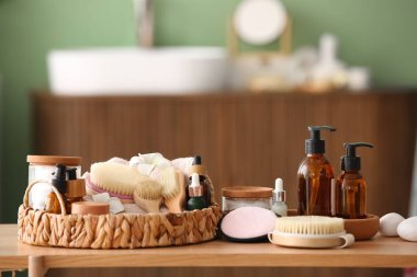 Wicker tepsisi, farklı spa aksesuarları ve kozmetik ürünleri banyodaki ahşap masada.