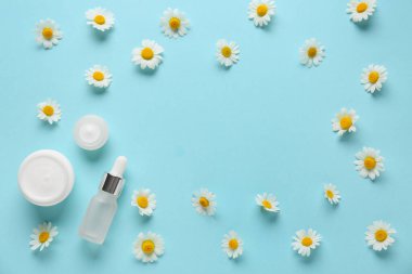 Mavi arka planda papatya çayı kozmetik kremi, çiçek ve yağ dolu kavanozlardan yapılmış çerçeve.